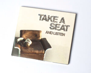CD Cover Take a Seat and listen, typografie und brauner Miniaturstuhl, Braun Design mit Miniatur Kopfhörer