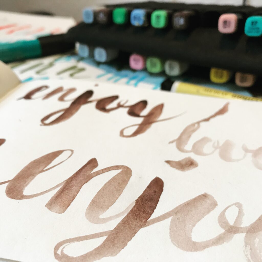 Close Up von Kalligrafie "enjoy" und Copic Marker im Hintergrund