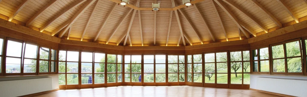 großer achteckiger Seminarraum mit Holzboden und Panoramafenstern ins Grüne